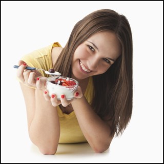 Studio portrait of young woman eating strawberries and yogurt. Photo : Mike Kemp