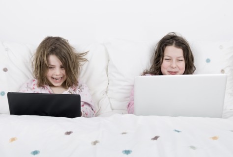 Girls (6-7,8-9) with laptops sitting in bed. Photo : Justin Paget