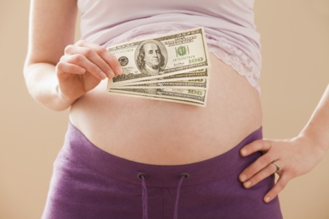 Young pregnant woman holding money roll of dollars. Photo : Mike Kemp