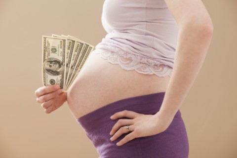 Young pregnant woman holding money roll of Dollars. Photo : Mike Kemp