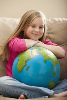 Cheerful girl (8-9) sitting on sofa with globe on knees. Photo: Mike Kemp