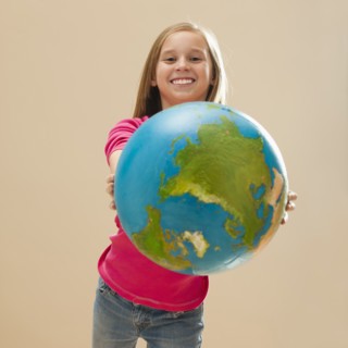 Studio portrait of girl (8-9) holding globe. Photo : Mike Kemp