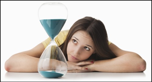 Young woman watching hourglass. Photo : Mike Kemp