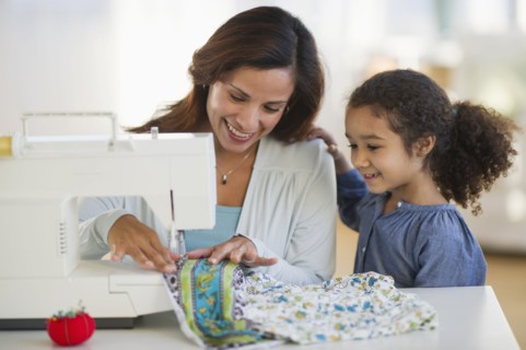 Mother with daughter (6-7) using sewing machine.