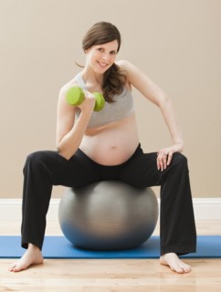 Young pregnant woman exercising with dumbbells and fitness ball. Photo : Mike Kemp