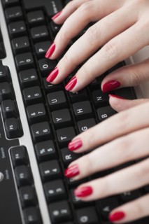 Close up of woman's fingers with red nail polish typing on computer keyboard.