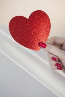 Close up of woman's fingers with red nail polish holding red heart.