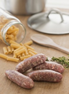Raw sausage and pasta on kitchen table.
