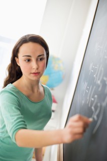 Teenage girl (14-15) writing on blackboard.