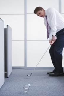 Businessman playing golf at office. Photo : Daniel Grill