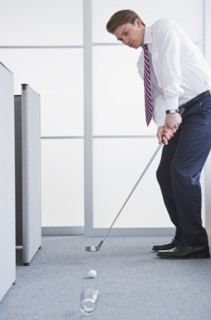 Businessman playing golf at office. Photo : Daniel Grill