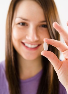 Portrait of smiling young woman holding pill. Photo : Jamie Grill Photography