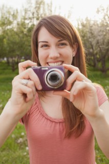 USA, Utah, Provo, Young woman holding digital camera in orchard. Photo : Mike Kemp