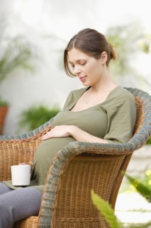 Pregnant woman sitting in wicker chair, touching belly. Photo : Rob Lewine