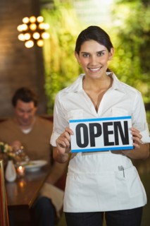 Smiling waitress in restaurant showing "open sign".