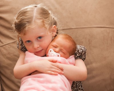 Portrait of girl (2-3) holding newborn girl (0-1months) . Photo : Mike Kemp