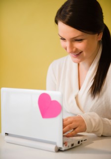 Smiling young woman using laptop with pink heart. Photo : Jamie Grill Photography