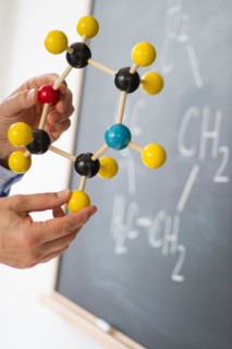 Close-up of man's hands holding molecule model, blackboard in background.