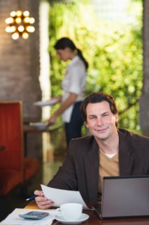 Owner working with laptop in restaurant with waitress in background.