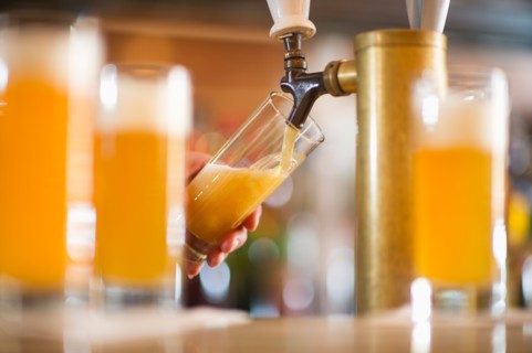 Barman poring beer from beer tap .