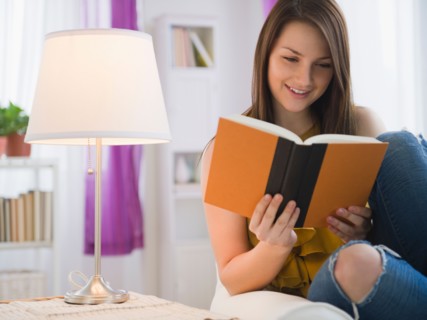 Young woman reading book in living room. Photo : Jamie Grill Photography