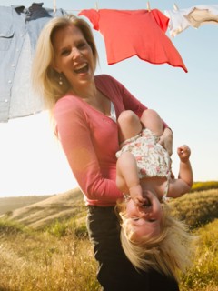 Mother playing with daughter (12-17 months) with laundry on clothesline in background.