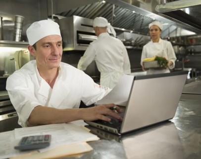 Chefs preparing food, one working on laptop.