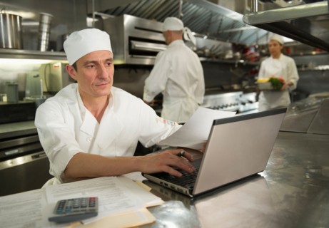 Chefs preparing food, one working on laptop.