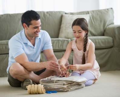 Father and daughter (8-9) wrapping up wastepaper bundle.