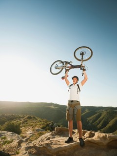 USA, California, Laguna Beach, Mountain biker on top of hill holding up his bike.