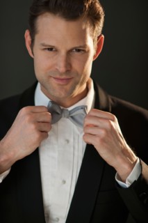 Studio portrait of bridegroom adjusting bow tie.