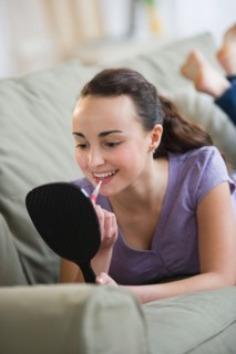 Teenage girl (14-15) applying lipstick.
