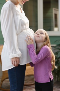 Girl (4-5) putting ear to expectant mother's belly. Photo : Rob Lewine