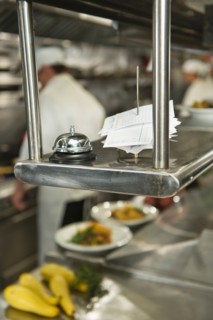 Chefs preparing food in kitchen, focus on service bell on foreground.