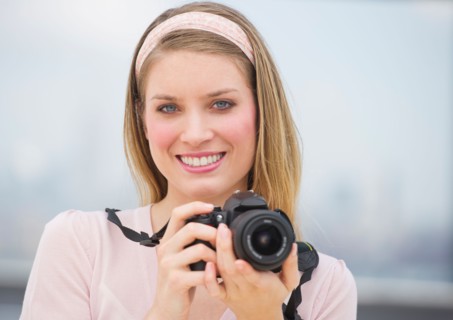 Portrait of young woman holding camera, smiling.