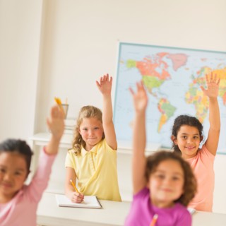 Four girls (6-9) raising hands in classroom.
