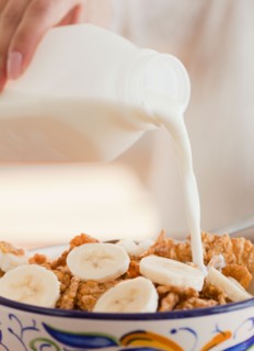 Close up of hand pouring milk into bowl of cereals. Photo : Jamie Grill