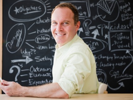 Businessman sitting at table against blackboard. Photo : Jamie Grill