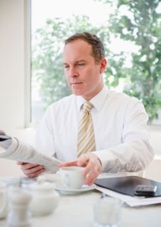 Businessman reading newspaper at table. Photo : Jamie Grill