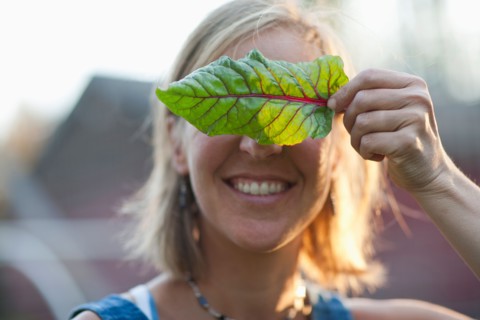 Smiling woman holding leaf in front of her face. Photo : Noah Clayton