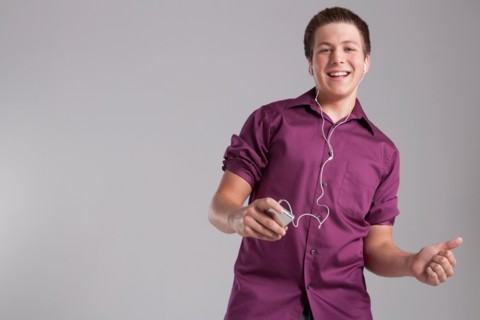 Portrait of smiling teenager listening mp3 player, studio shot. Photo: Rob Lewine