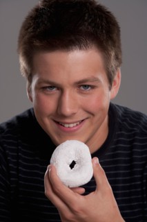Portrait of teenage boy (16-17) with donut, studio shot. Photo: Rob Lewine
