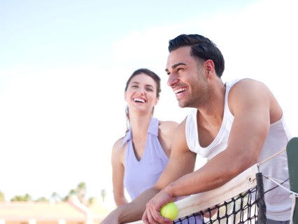 Smiling couple standing near tennis net. Photo : db2stock