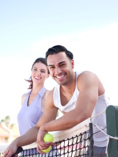 Smiling couple standing near tennis net. Photo : db2stock