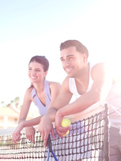 Smiling couple standing near tennis net. Photo : db2stock