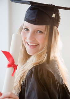 Young woman wearing graduation gown with diploma. Photo : Jamie Grill