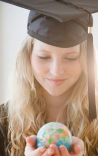 Woman wearing graduation gown holding small globe. Photo : Jamie Grill