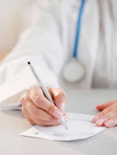 Close up of female doctor's hands writing prescription. Photo : Jamie Grill
