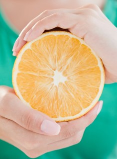 Close up of woman's hands holding half of orange. Photo : Jamie Grill