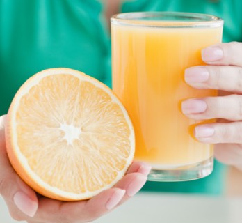 Close up of woman's hands holding half of orange and glass of juice. Photo : Jamie Grill